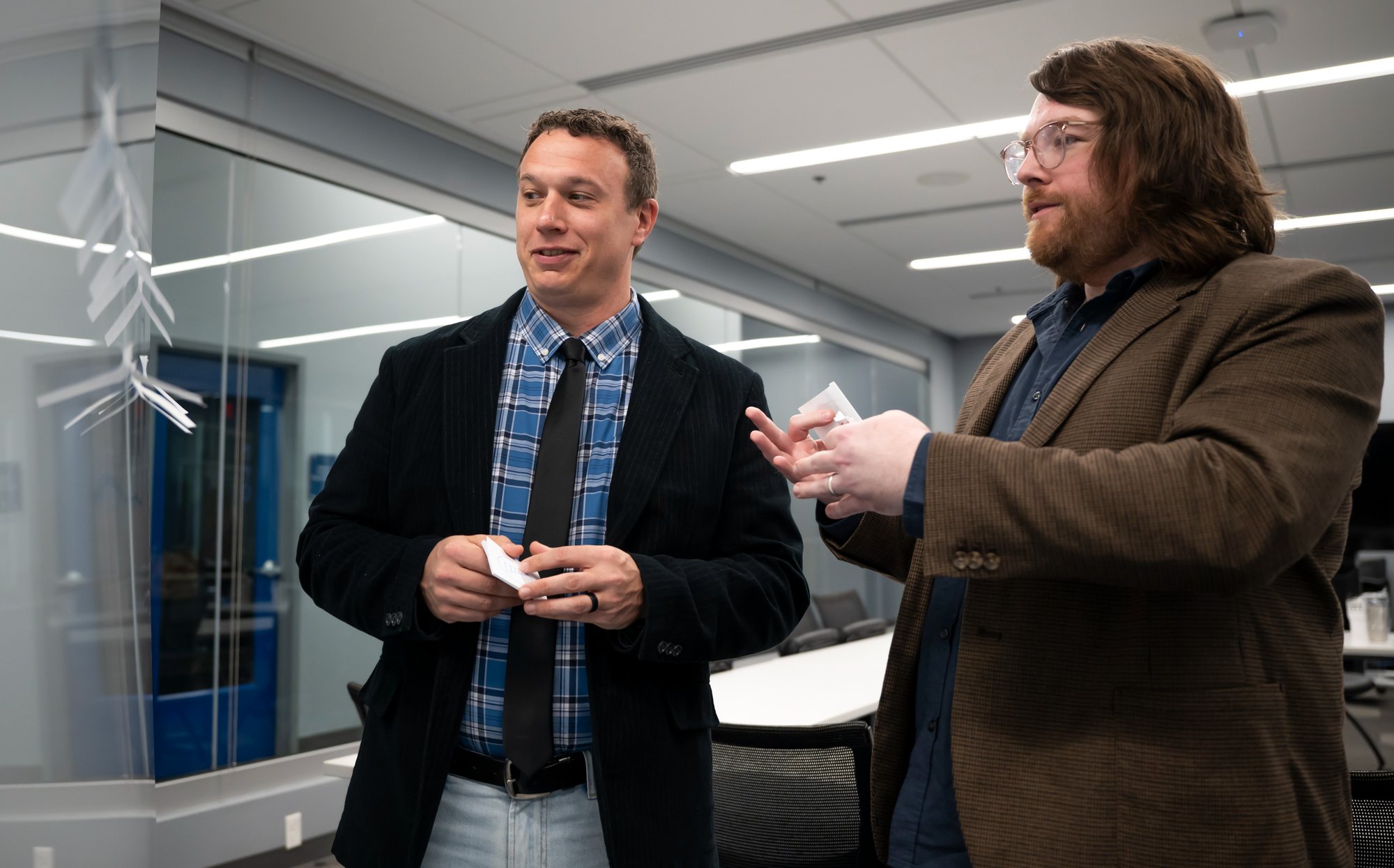 Two professionals standing in a conference room and talking during a learning or training session, each holding a small object in their hands.